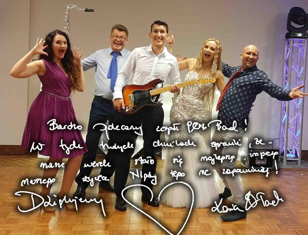 Uśmiechnięta grupa muzyków w różnym wieku, w strojach estradowych, pozuje z instrumentami na tle oświetlenia scenicznego i podziękowaniami dla zespołu naniesionymi na zdjęcie.