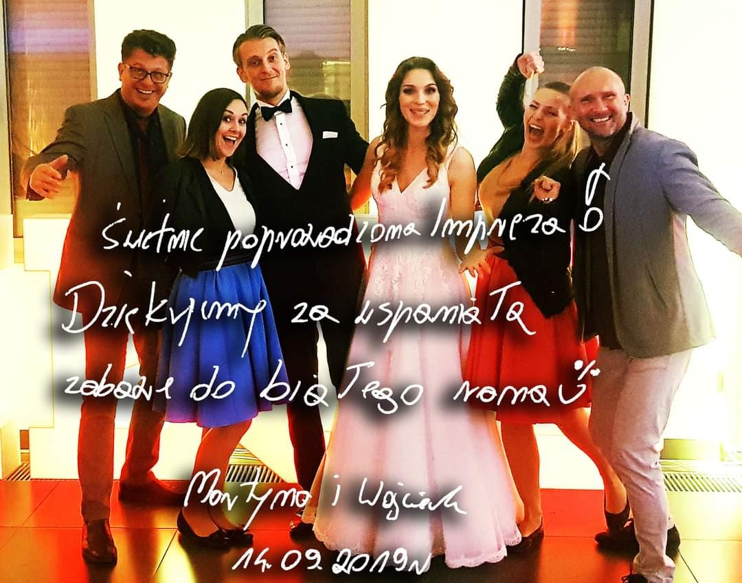 Uśmiechnięta grupa osób, prawdopodobnie wykonawców muzycznych i gości, pozuje do zdjęcia na tle jasnej ściany podczas imprezy. Na pierwszym planie widoczny biały napis z podziękowaniem za udaną...