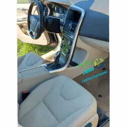 Wnętrze samochodu Volvo po czyszczeniu, beżowa skórzana tapicerka foteli i deski rozdzielczej, widoczny fragment szyby i zielona trawa w tle, logo firmy Perfect Clean nałożone na zdjęcie.