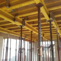 Szczegółowe ujęcie szalunku stropowego z żółtymi belkami i stalowymi podporami, widoczne oznaczenia producenta PERI na belkach, ściany z bloczków betonu komórkowego w tle.