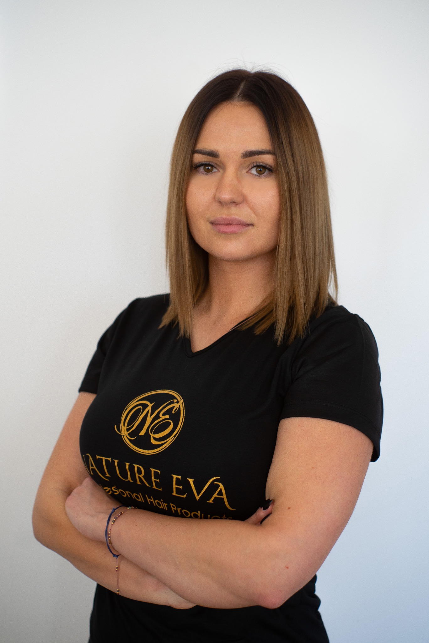 Portret kobiety z brązowymi włosami do ramion, ubrana w czarną koszulkę z logo Nature Eva, pozująca na jasnym tle z założonymi rękami.