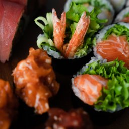Sushi Kado - Różnorodne sushi: rolki z tuńczykiem, łososiem i krewetkami, udekorowane sałatą i ogórkiem, podane na ciemnym tle.