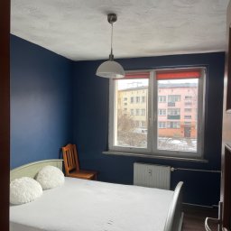 Filip Tuszyński FIL-BUD Usługi Ogólnobudowlane - Ściana pomalowana na ciemny niebieski kolor w pokoju w Nysie, widoczny grzejnik pod oknem i wzorzysty sufit.