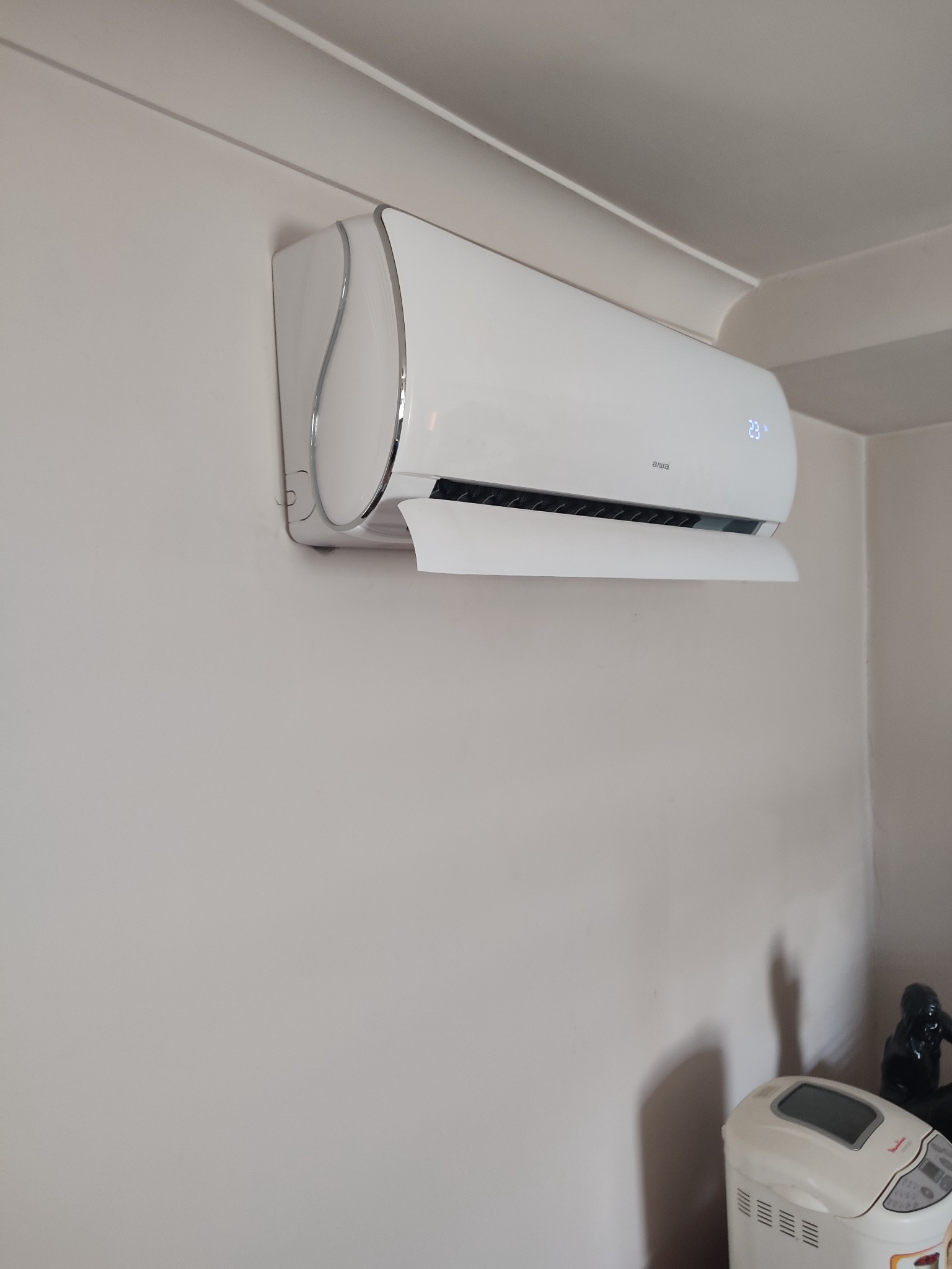 Zamontowana klimatyzacja marki Aiwa z wyświetlaną temperaturą 23 stopnie Celsjusza na ścianie w domu w miejscowości Suków. Widoczny fragment automatu do pieczenia chleba.