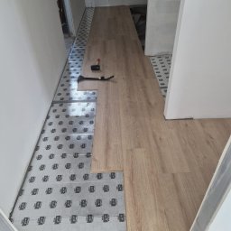 Darlbud Mateusz Dul - Układanie paneli podłogowych na folii izolacyjnej z użyciem gumowego młotka i dobijaka w trakcie remontu korytarza.