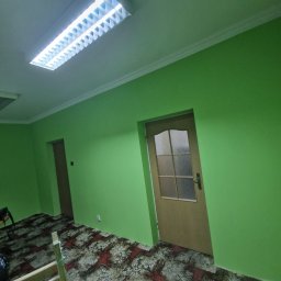 Darlbud Mateusz Dul - Świeżo pomalowane na zielono wnętrze w Woli Raniżowskiej z widoczną drewnianą ościeżnicą drzwi i wzorzystą podłogą, oświetlone jasnym światłem z lampy sufitowej.