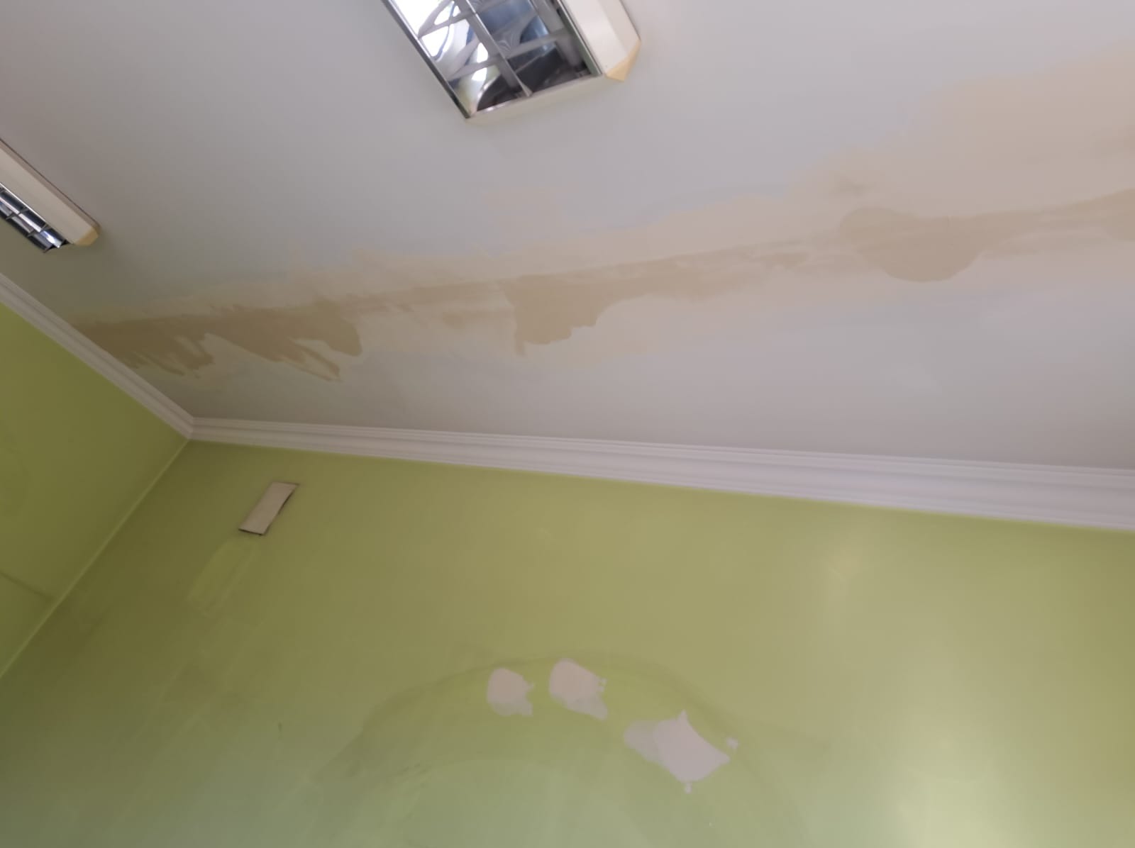 Zacieki na suficie i ścianie w odcieniach beżu i zieleni, widoczny fragment oświetlenia sufitowego.