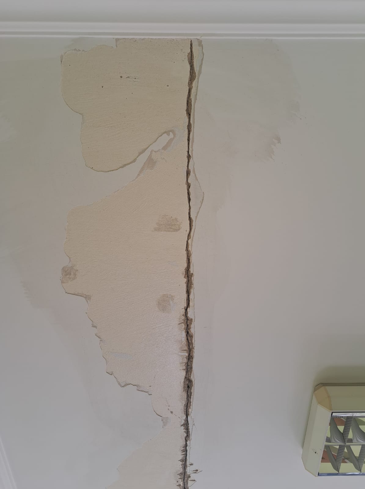 Pęknięcie na suficie z widocznymi śladami po naprawie, częściowo pokryte masą szpachlową, ukazujące etap prac remontowych.