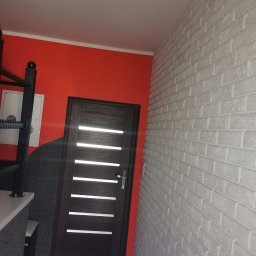 Dar-but firma handlowo usługowa Dariusz Czajkowski - Wnętrze z pomarańczową ścianą, szarą ścianą z efektem kamienia, ciemnymi drzwiami z poziomymi przeszkleniami i białą ścianą z cegieł.