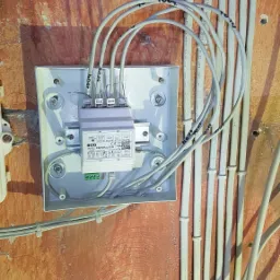 Rozdzielnica alarmowa ACO CDNVRau-DIN w białej obudowie na pomarańczowej ścianie z poprowadzonymi szarymi kablami oznaczonymi numerami, widoczne również rury instalacyjne przytwierdzone do ściany.