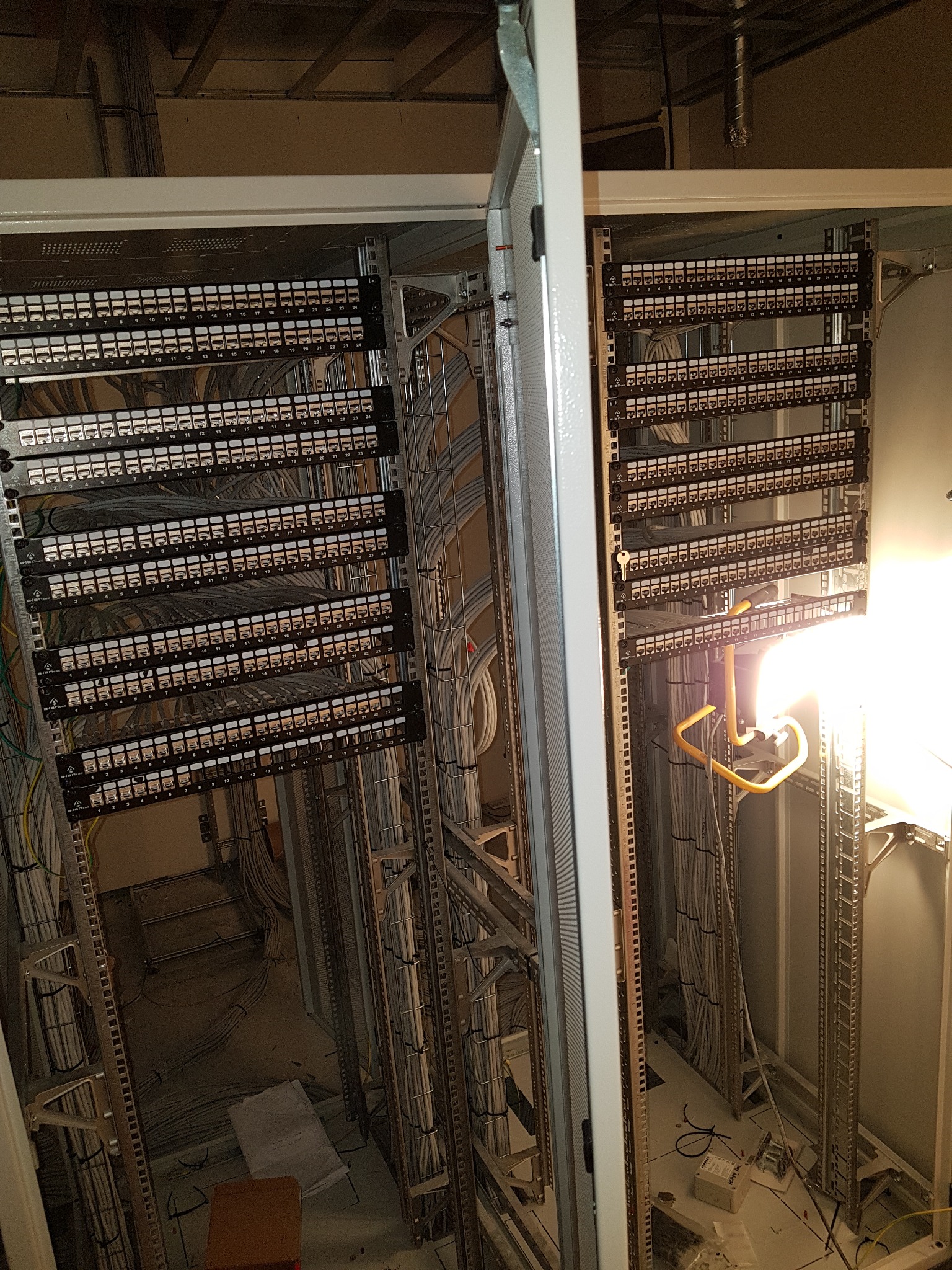 Rozdzielnica elektryczna z licznymi portami Ethernet, kable uporządkowane w korytkach, widoczne detale montażu wewnątrz szafy, oświetlenie halogenowe podkreśla infrastrukturę.