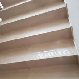 Kremowe, błyszczące schody wyłożone płytkami ceramicznymi z delikatnym wzorem poziomych linii, widoczne z dołu pod kątem, ukazujące świeżo umytą powierzchnię.