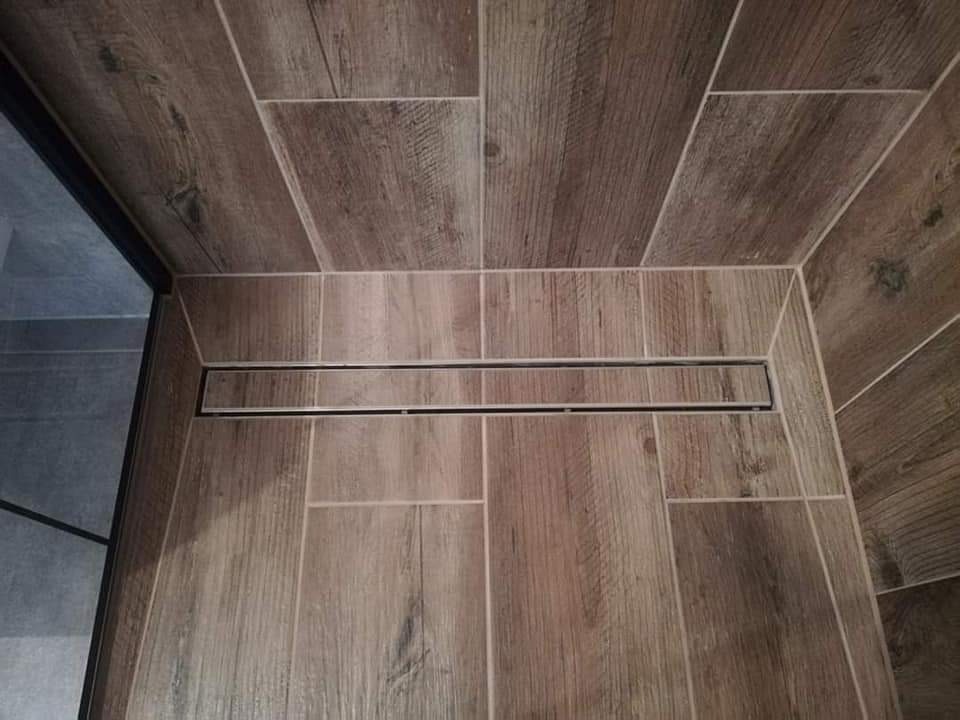 Ukośne ułożenie płytek imitujących drewno na podłodze i ścianie kabiny prysznicowej, z odpływem liniowym wzdłuż ściany, widok z góry.