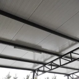 Widok od dołu na białe panele dachowe zamocowane do czarnej stalowej konstrukcji nośnej z oświetleniem liniowym LED.