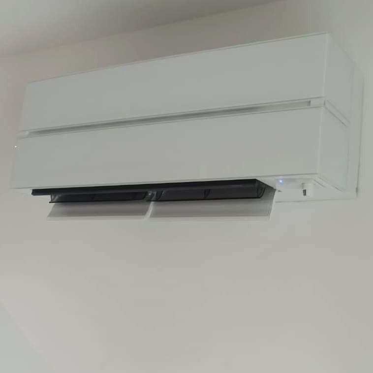 Biały klimatyzator ścienny z otwartymi żaluzjami, widoczna niebieska dioda LED, zamontowany na gładkiej, jasnej ścianie.