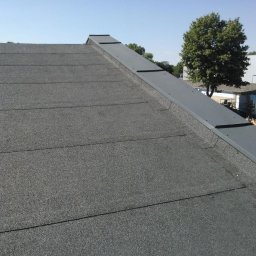 Przemysław Czerko - Dach pokryty papą termozgrzewalną z metalowym obrzeżem, widok z góry na ukośną powierzchnię, w tle drzewo i budynek przemysłowy.