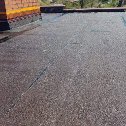 Przemysław Czerko - Widok z góry na płaski dach pokryty papą z widocznym kominem i śladami wilgoci wzdłuż łączeń.