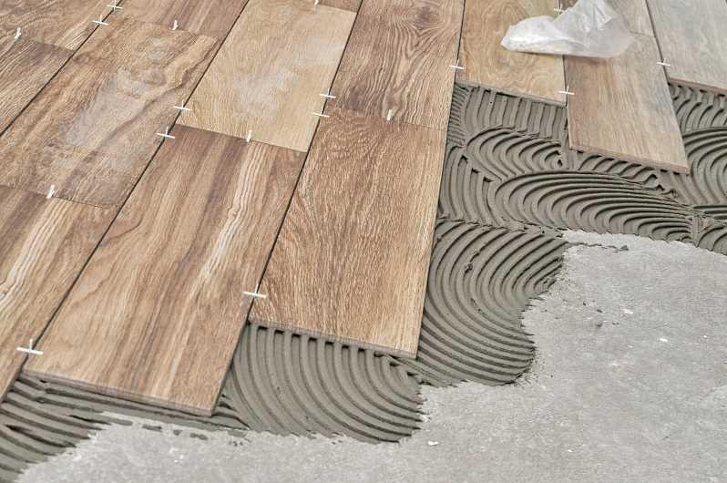 Układanie drewnopodobnych płytek podłogowych z użyciem krzyżyków dystansowych i świeżo nałożonej zaprawy klejowej, widoczne charakterystyczne żłobienia zaprawy.