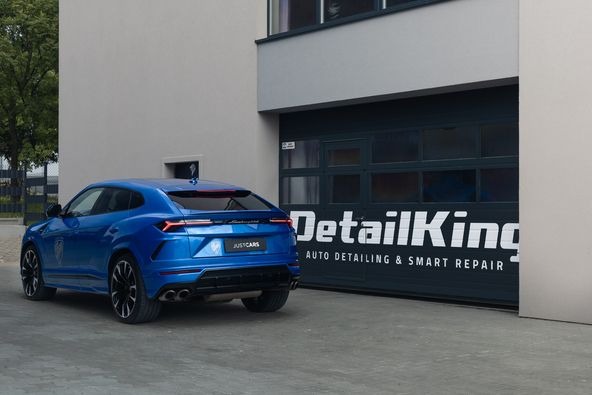 Błękitny Lamborghini Urus zaparkowany przed garażem z napisem 'DetailKing Auto Detailing & Smart Repair'.