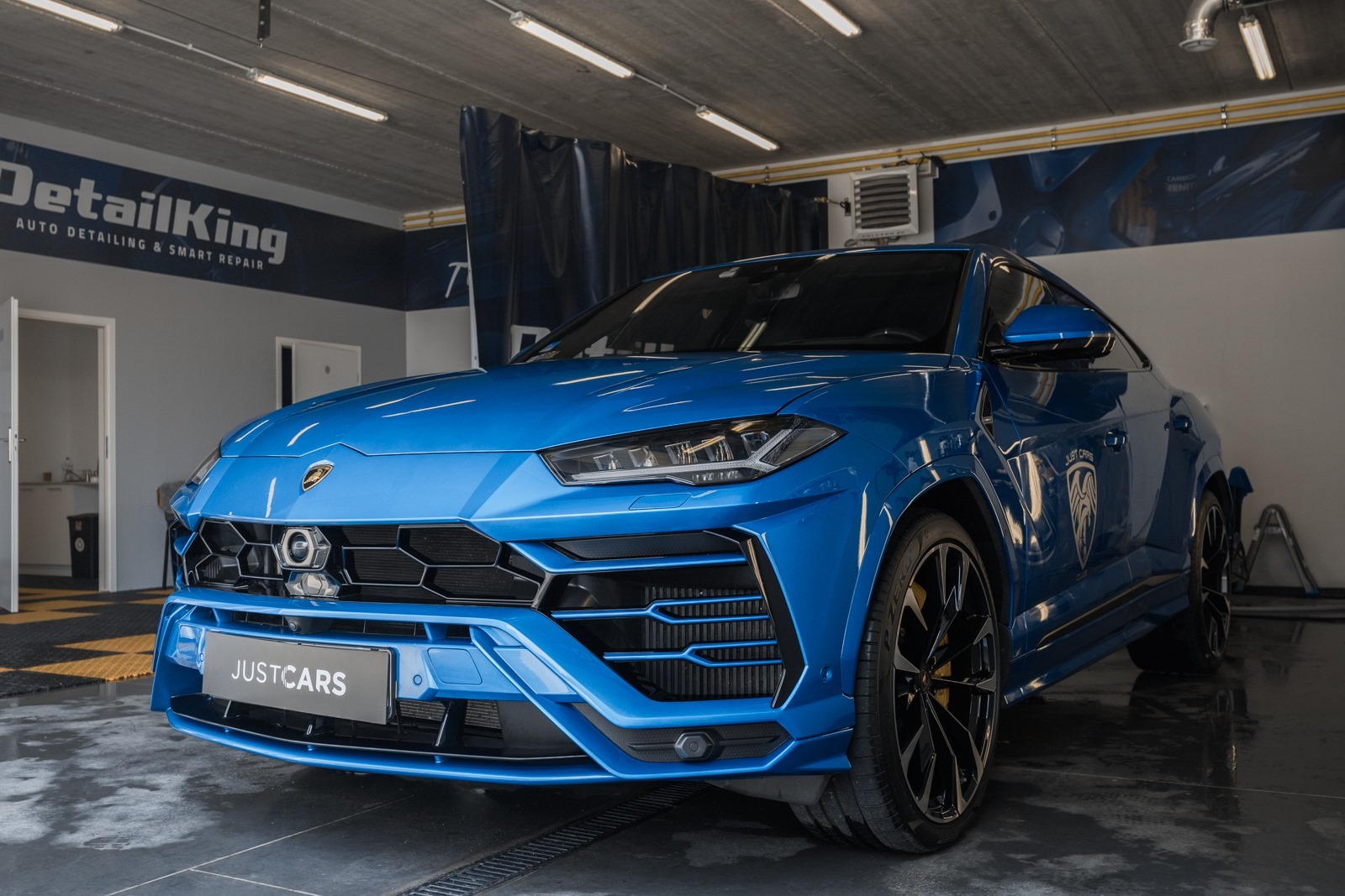 Błękitny Lamborghini Urus po detailingu, widoczny z przodu, z logo DetailKing w tle i tablicą rejestracyjną JUSTCARS.