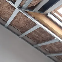 Szkielet metalowy pod sufit z wełną mineralną, widok z dołu, fragment okna dachowego w tle.
