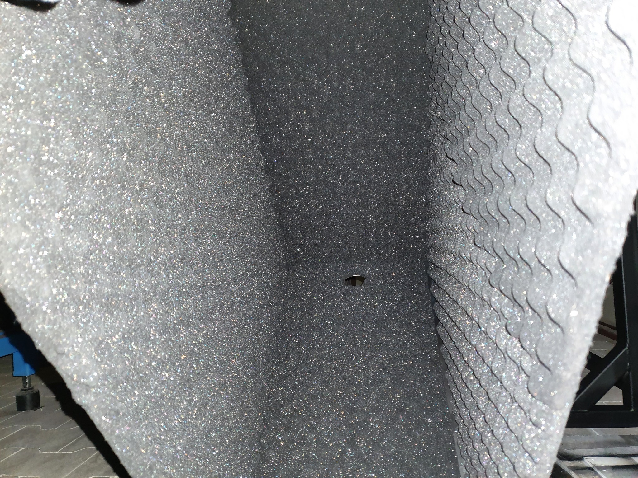 Wnętrze komory z wygłuszającą pianką akustyczną o nieregularnej strukturze, widoczny otwór montażowy i fragment stalowej ramy konstrukcyjnej.