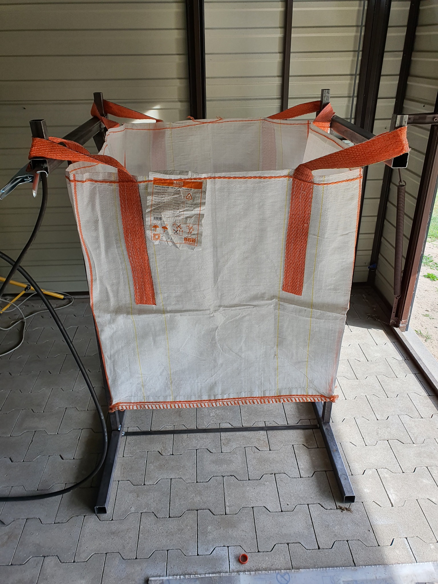 Stelaż z profili stalowych pod duży worek typu Big Bag z pomarańczowymi uchwytami, spawany w garażu.