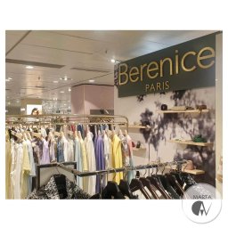 MartaGav Design - Wnętrze sklepu odzieżowego Berenice Paris z ubraniami pastelowymi na wieszakach i półkami z akcesoriami na ścianie, widoczne oświetlenie sufitowe i logo firmy