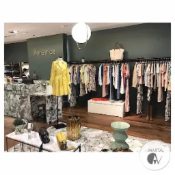 Wnętrze butiku odzieżowego z marmurową ladą, ubraniami na wieszakach i manekinem w żółtej sukience, oświetlone kulistą lampą.