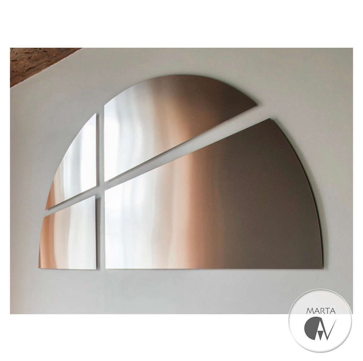 Metalowa dekoracja ścienna w kształcie półkola podzielonego na cztery części, z efektem lustrzanego odbicia i gradientem kolorów, umieszczona na białej ścianie, z logo firmy w prawym dolnym rogu.