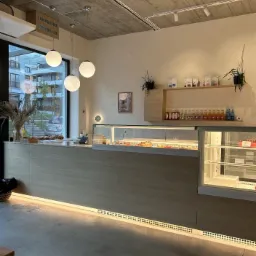 Nowoczesne wnętrze kawiarni z oświetlonym ladą, przeszkloną witryną z deserami i minimalistycznymi półkami na ścianie z napojami i kawami.