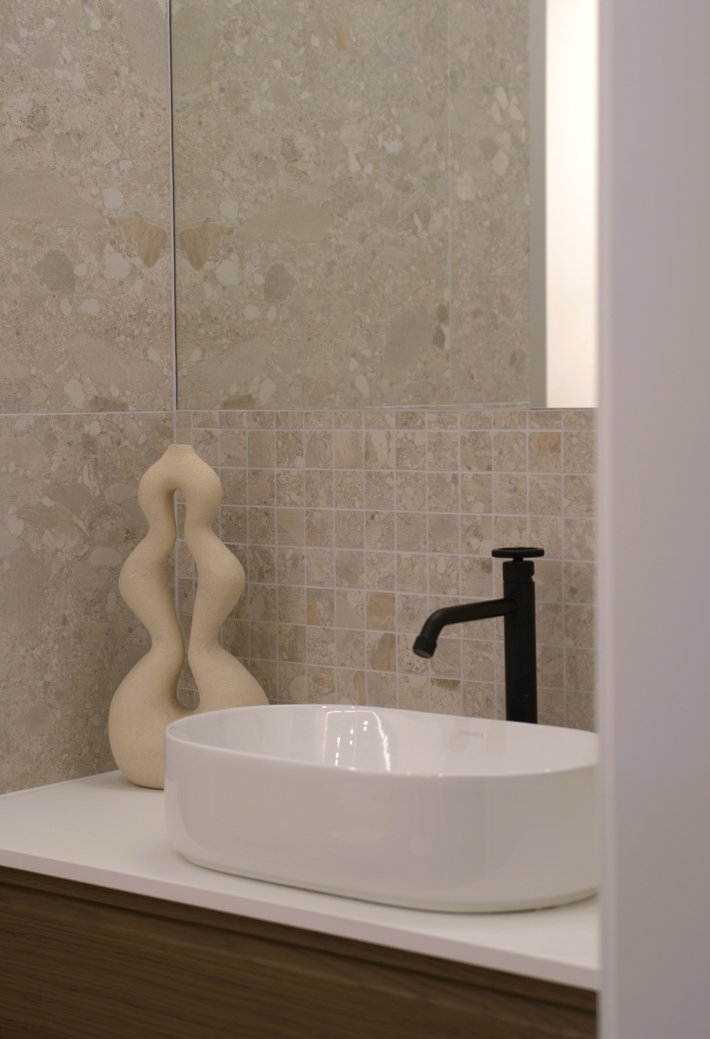 Stylowa umywalka nablatowa z czarną armaturą na tle mozaiki i płytek w beżowych odcieniach. Obok dekoracyjna, kremowa rzeźba.