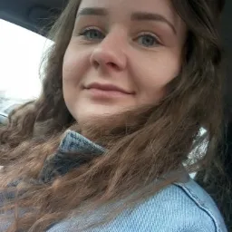 Portret kobiety z kręconymi włosami w samochodzie podczas deszczu, widoczne krople na szybie.