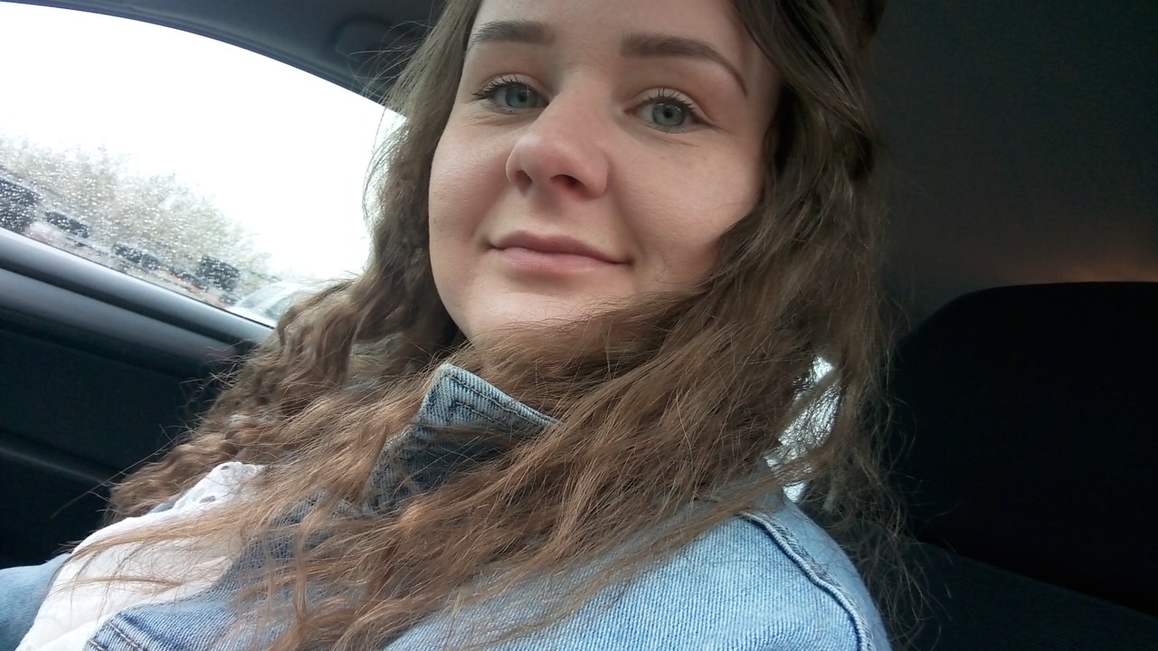 Portret kobiety z kręconymi włosami w samochodzie podczas deszczu, widoczne krople na szybie.