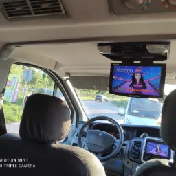 Wnętrze vana z widokiem na drogę przez przednią szybę; ekrany LCD wyświetlają animację dla pasażerów z tyłu, zamontowane na suficie i w desce rozdzielczej.