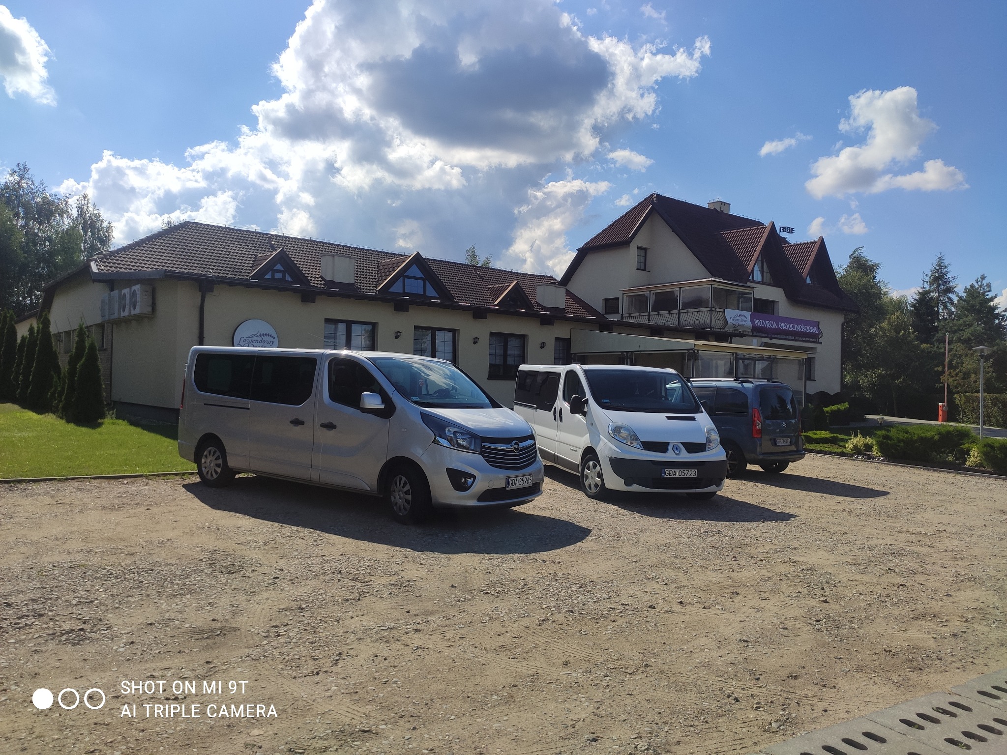 Trzy busy (srebrny, biały i granatowy) zaparkowane przed budynkiem z napisem 'Lawendowy Przyjęcia Okolicznościowe' w słoneczny dzień.