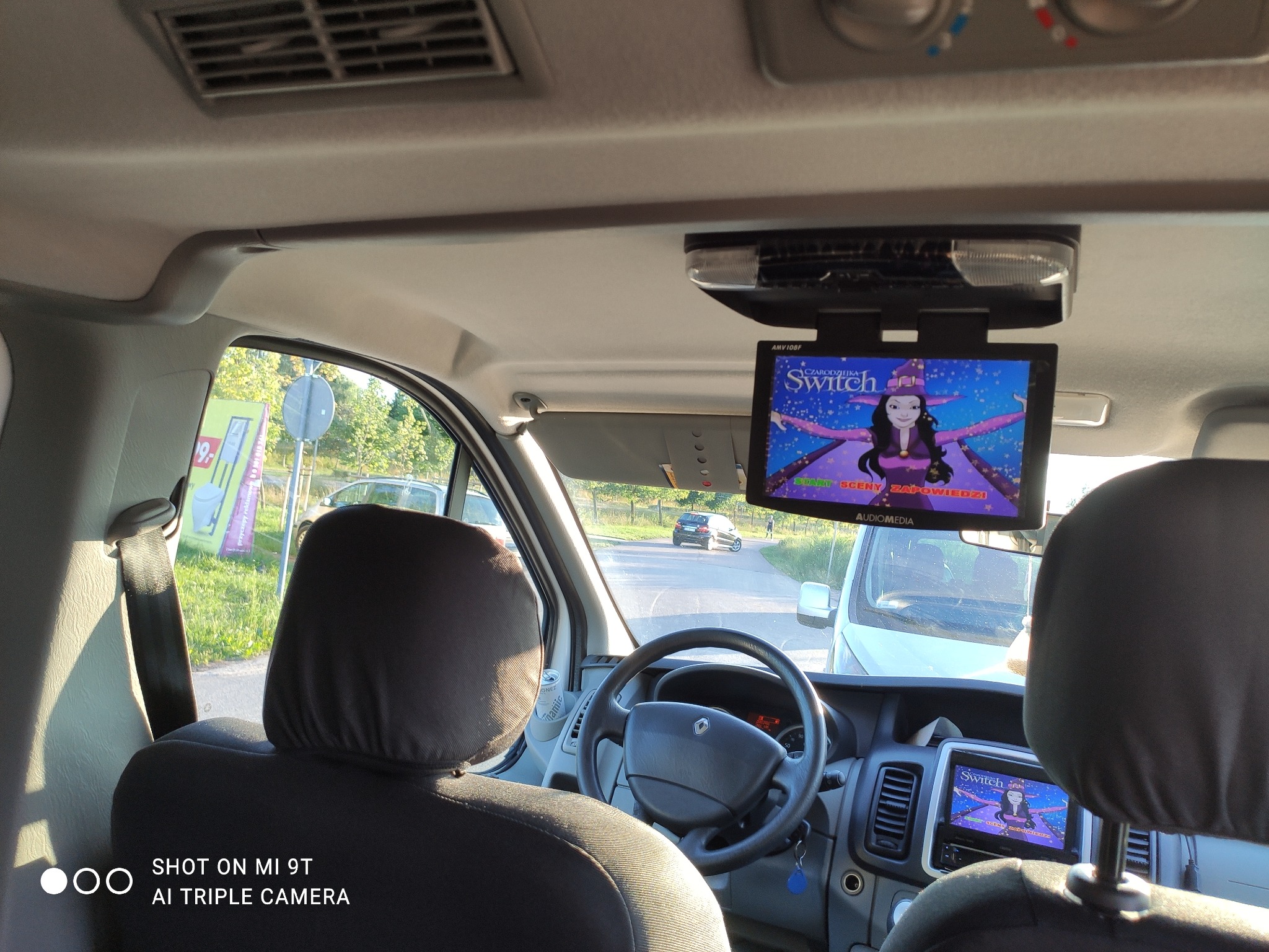 Wnętrze vana z widokiem na drogę przez przednią szybę; ekrany LCD wyświetlają animację dla pasażerów z tyłu, zamontowane na suficie i w desce rozdzielczej.