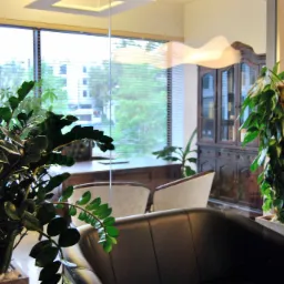 Eleganckie biuro z biurkiem, krzesłami, roślinami doniczkowymi i antycznym kredensem, widok przez szklaną ścianę na zieleń za oknem.