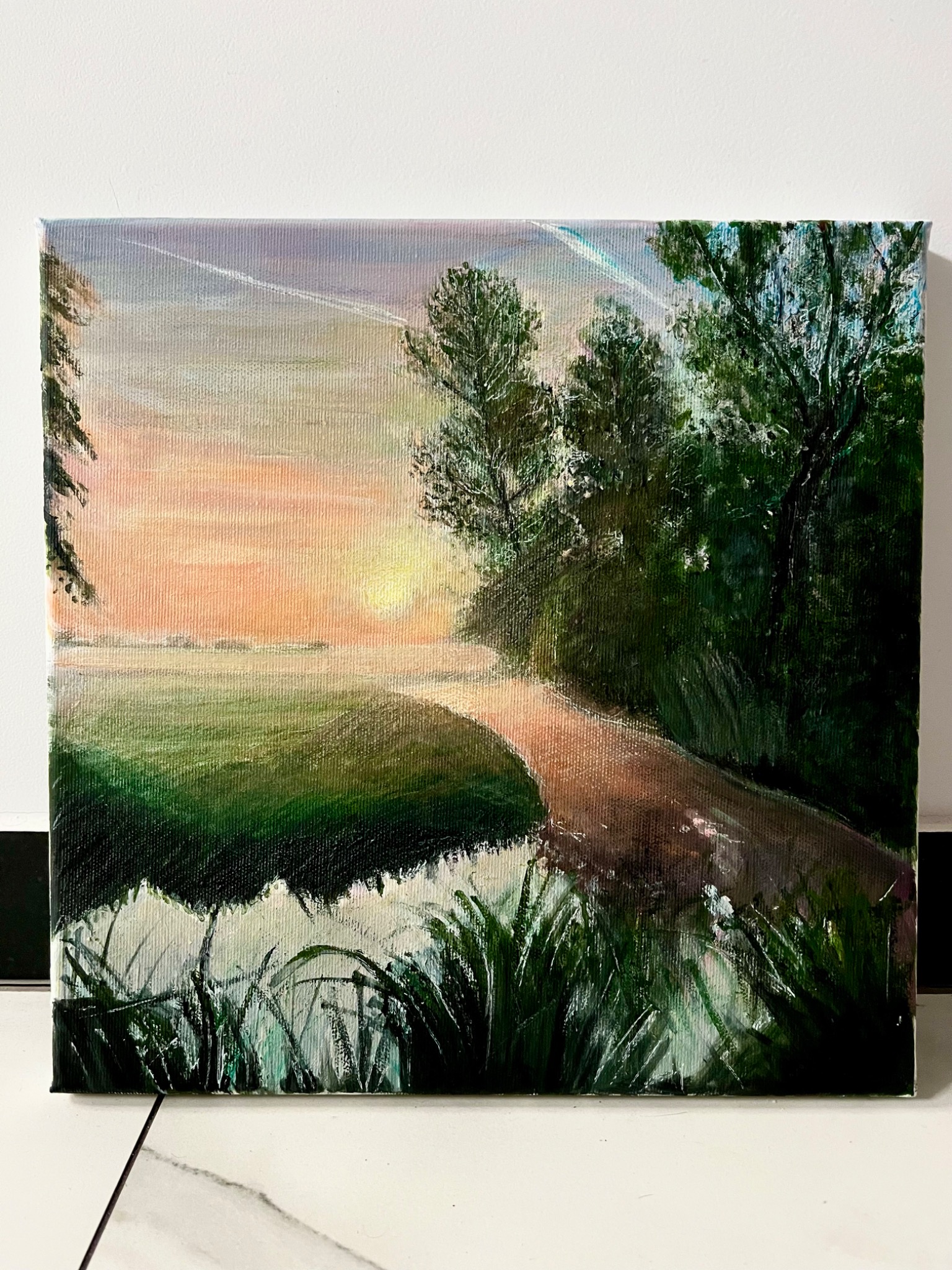 Pejzaż olejny na płótnie: zachód słońca nad wodą, zalesiony brzeg i trawy w pierwszym planie. Widoczne ślady pędzla, ciepłe barwy.