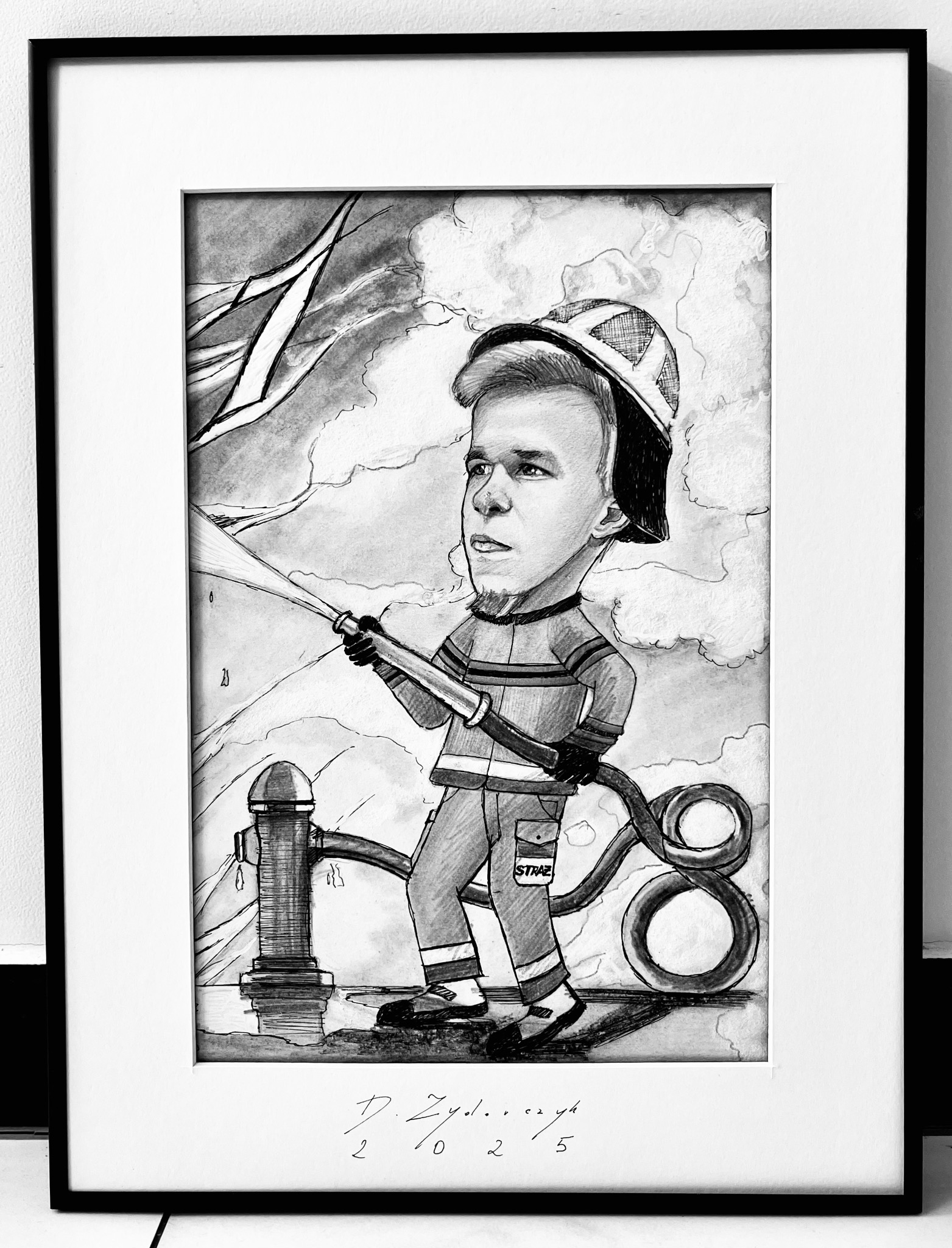 Czarno-biały, oprawiony rysunek karykaturalny strażaka z hełmem, trzymającego wąż strażacki, na tle chmur i hydrantu. Rysunek sygnowany.