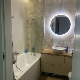 Reghome Sp. z o.o. - Nowoczesna łazienka z podświetlanym lustrem, umywalką nablatową i wanną z parawanem, wykończona płytkami w odcieniach beżu i brązu, oświetlenie LED podsufitowe.