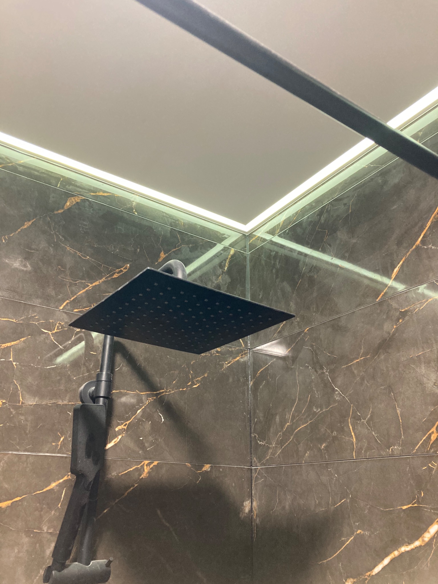 Nowoczesna kabina prysznicowa z czarną deszczownicą na tle płytek imitujących marmur z złotymi żyłami i podświetlanym sufitem.