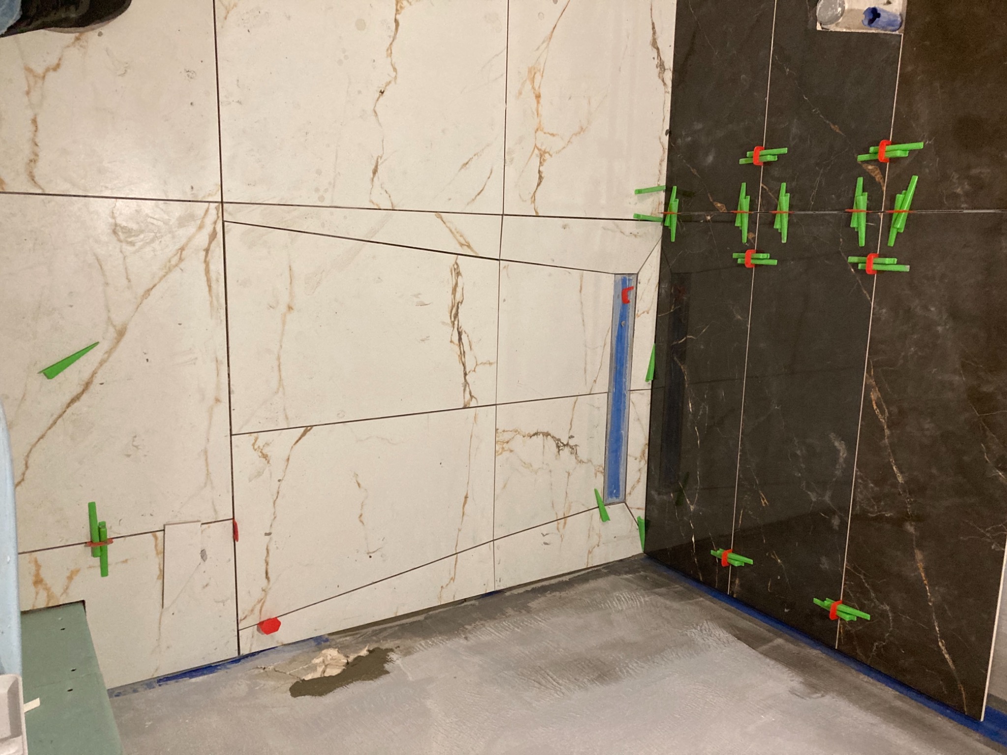 Układanie płytek imitujących marmur, jasnych i ciemnych, z użyciem klipsów poziomujących, widoczny fragment podłogi przed fugowaniem.