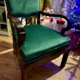 Odnowione krzesło z ciemnego drewna z zieloną, aksamitną tapicerką, ozdobione ćwiekami, na tle choinki i dekoracji świątecznych.