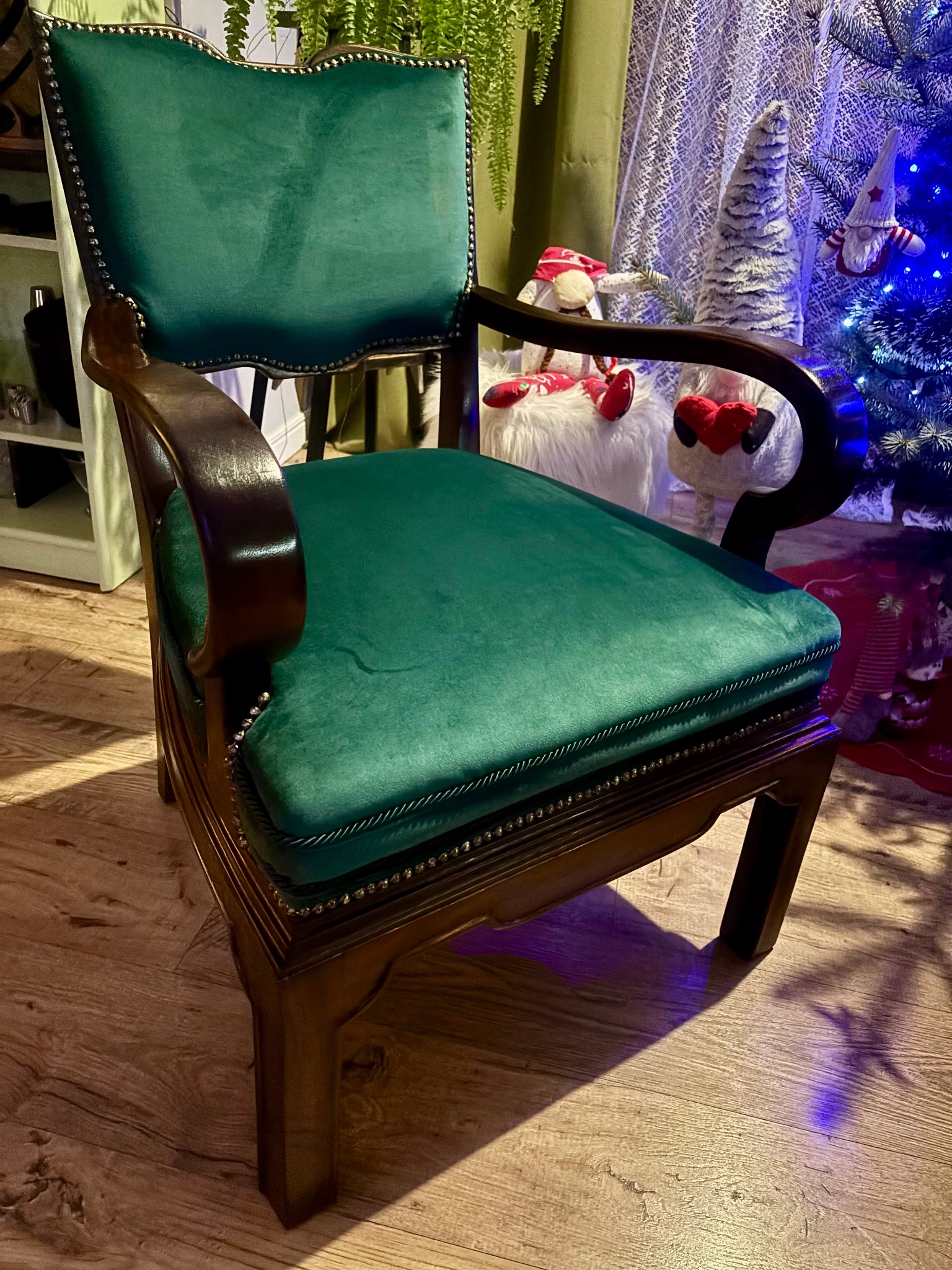 Odnowione krzesło z ciemnego drewna z zieloną, aksamitną tapicerką, ozdobione ćwiekami, na tle choinki i dekoracji świątecznych.