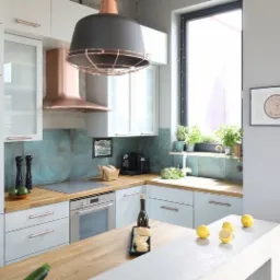 Jasna kuchnia w stylu loft z drewnianym blatem, miedzianymi akcentami i ozdobnym oświetleniem, na blacie leżą cytryny i butelka wina.