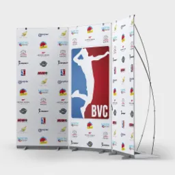 Trzy roll-upy reklamowe z logotypami różnych firm, w tym sportowych i spożywczych, ustawione na szarym tle.