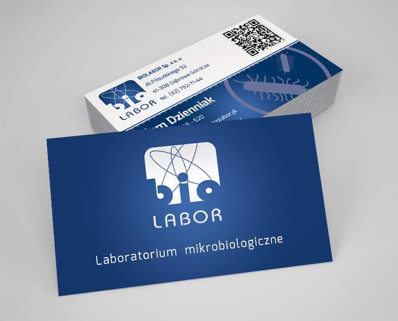 Stos wizytówek firmy BIOLABOR z logo przedstawiającym schemat atomu, na ciemnoniebieskim tle z napisem 'Laboratorium mikrobiologiczne' oraz QR kod na odwrocie.