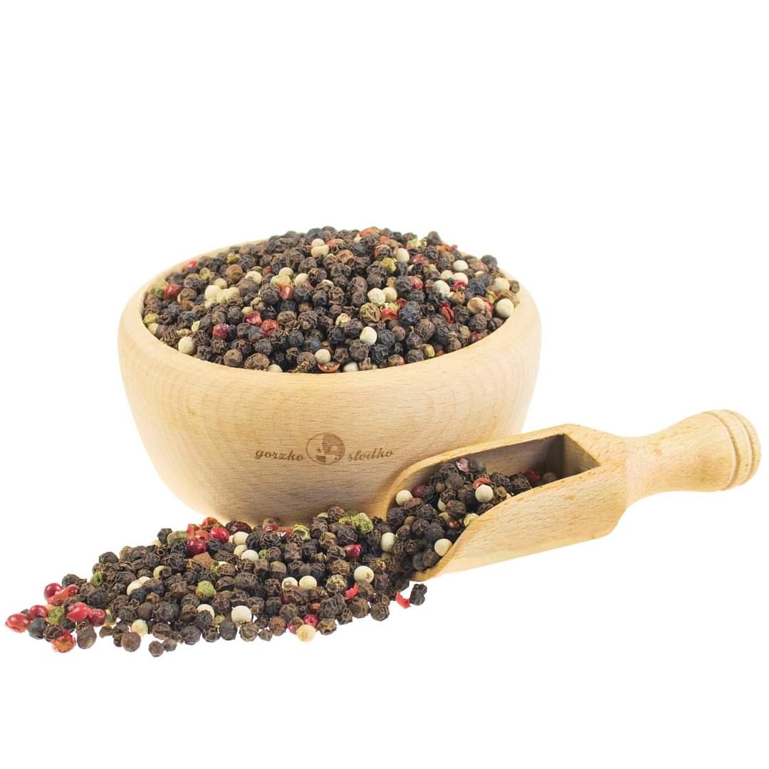 Mieszanka kolorowego pieprzu w drewnianej miseczce i nabierce na białym tle, widoczne ziarna czarnego, białego, zielonego i czerwonego pieprzu.