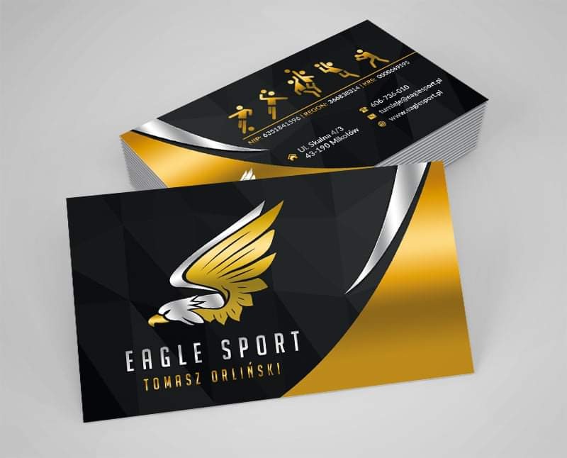 Stos wizytówek firmy Eagle Sport z logo złotego orła na czarno-złotym tle, obok wizytówka z danymi kontaktowymi i adresowymi.